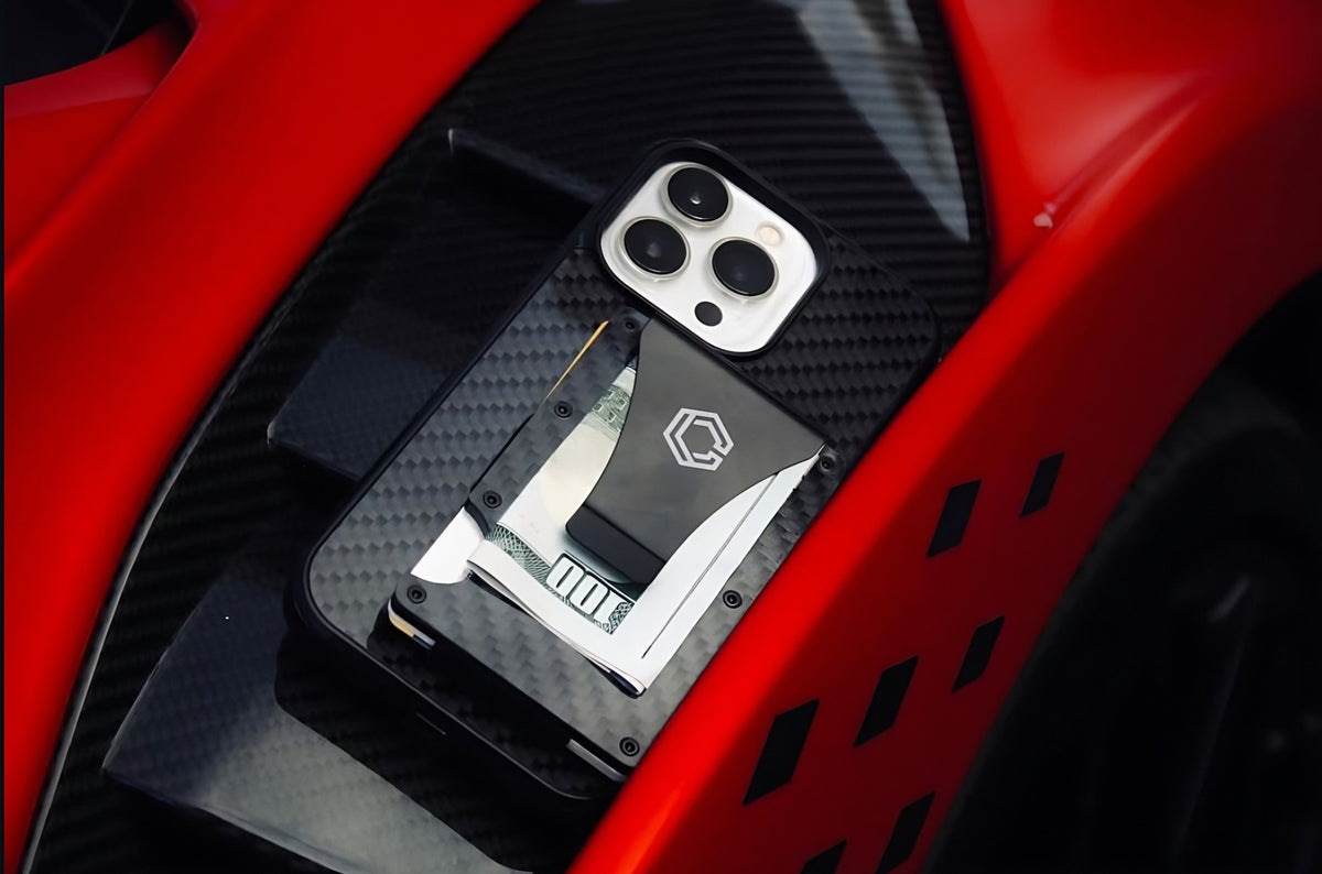 Carboluxe carbon fiber wallet with cash next to a phone in a carbon case, on a red car